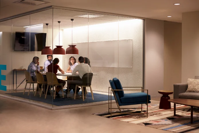 A team meeting in a glass-walled boardroom inside a coworking floor